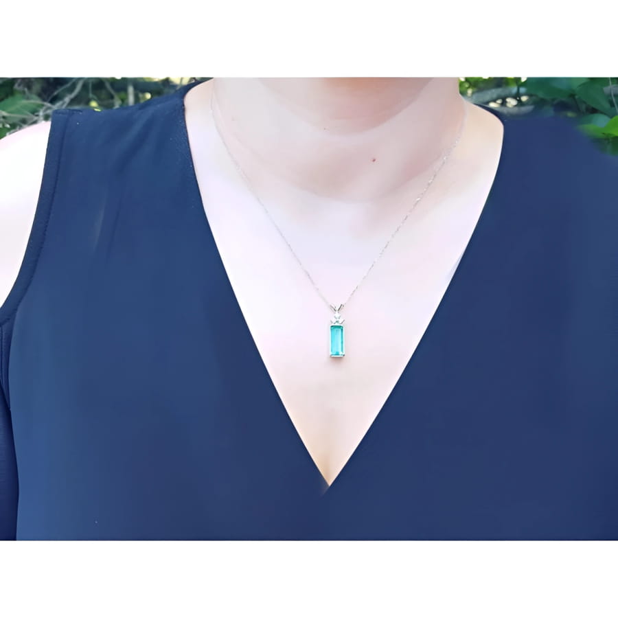 Emerald pendant with diamonds on a white gold chain, worn on a woman's neck.
