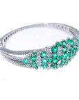 Right side profile view of a white gold bangle bracelet with round natural emeralds and diamonds on a white background.