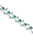 The side profile view of a white gold bracelet with round cut emeralds on a white background.