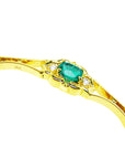 The side profile of a gold bracelet with a genuine emerald and diamonds on a white background.