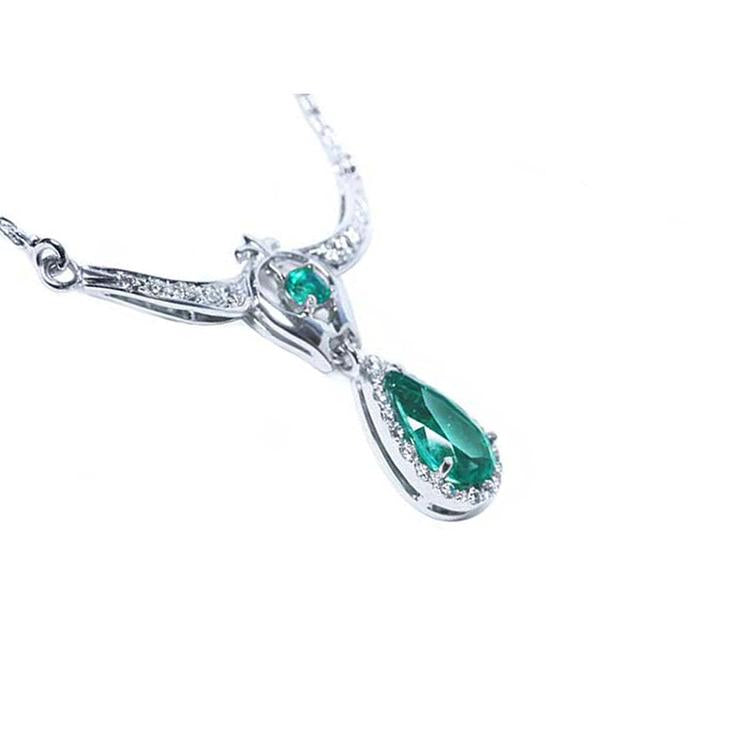 Side angle view of a white gold pear cut emerald halo diamond necklace on a white background