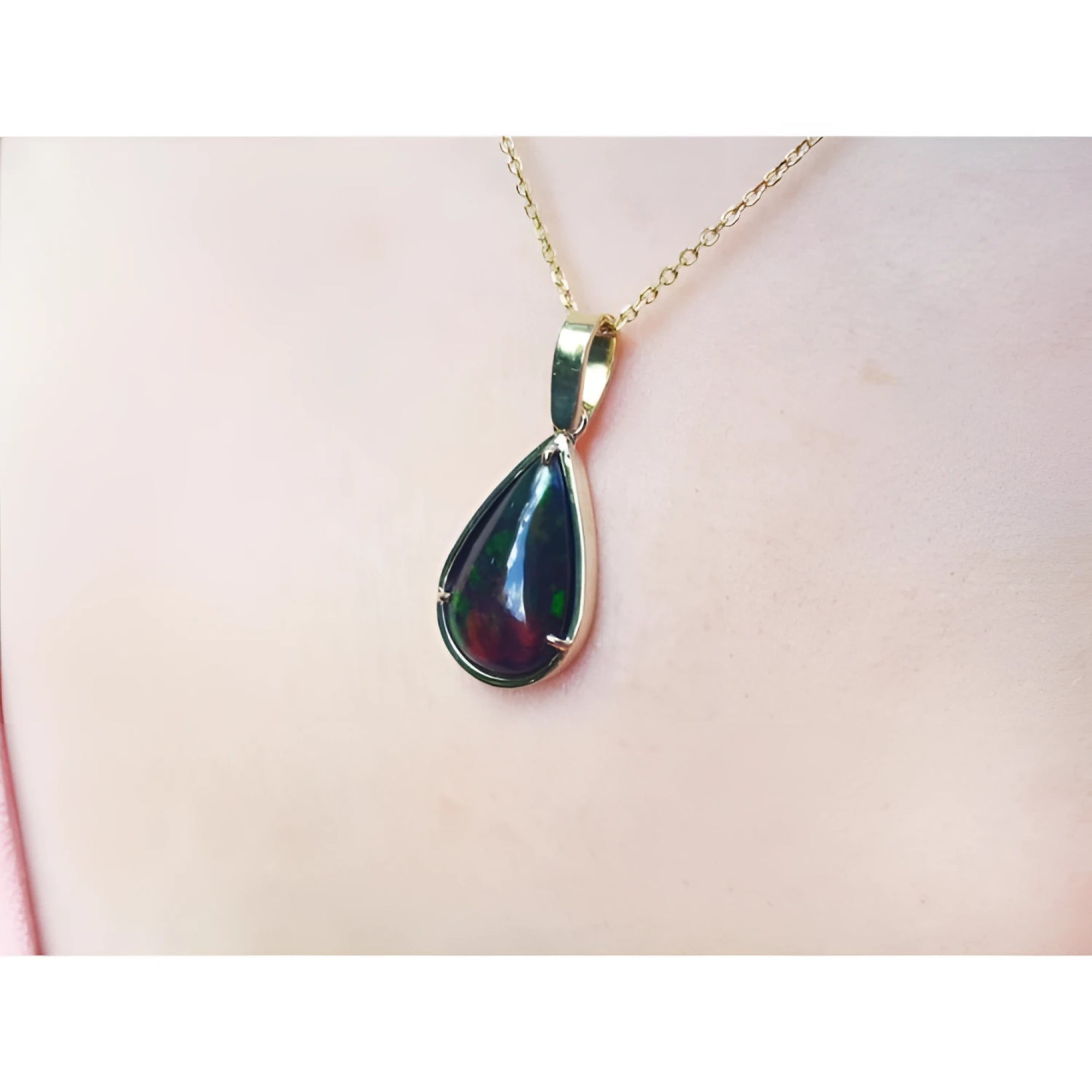 Teardrop Welo black opal pendant with red-orange and blue-green flashes on a 14K yellow gold chain.