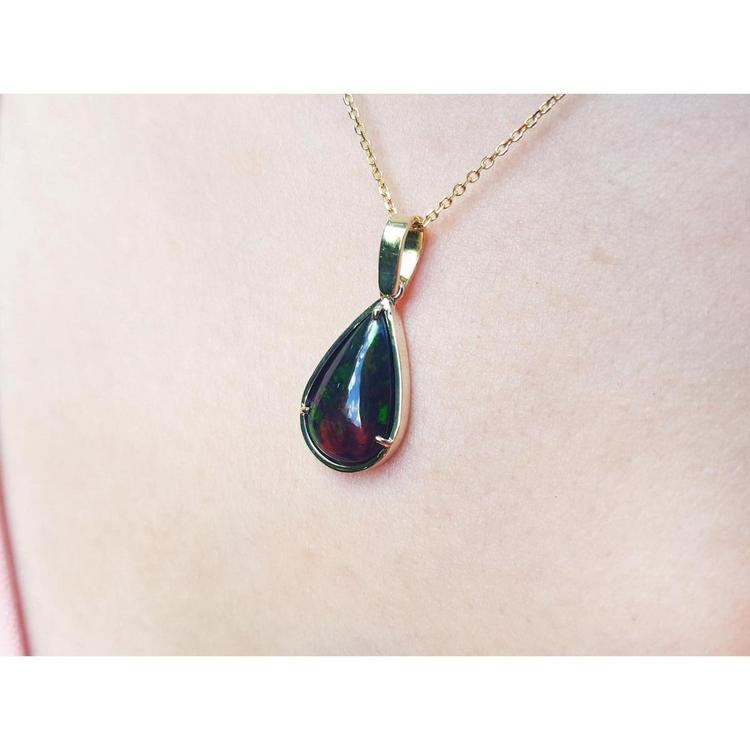 Teardrop Welo black opal pendant with red-orange and blue-green flashes on a 14K yellow gold chain.