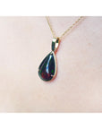 Teardrop-shaped opal pendant on a gold chain against a light pink skin background.
