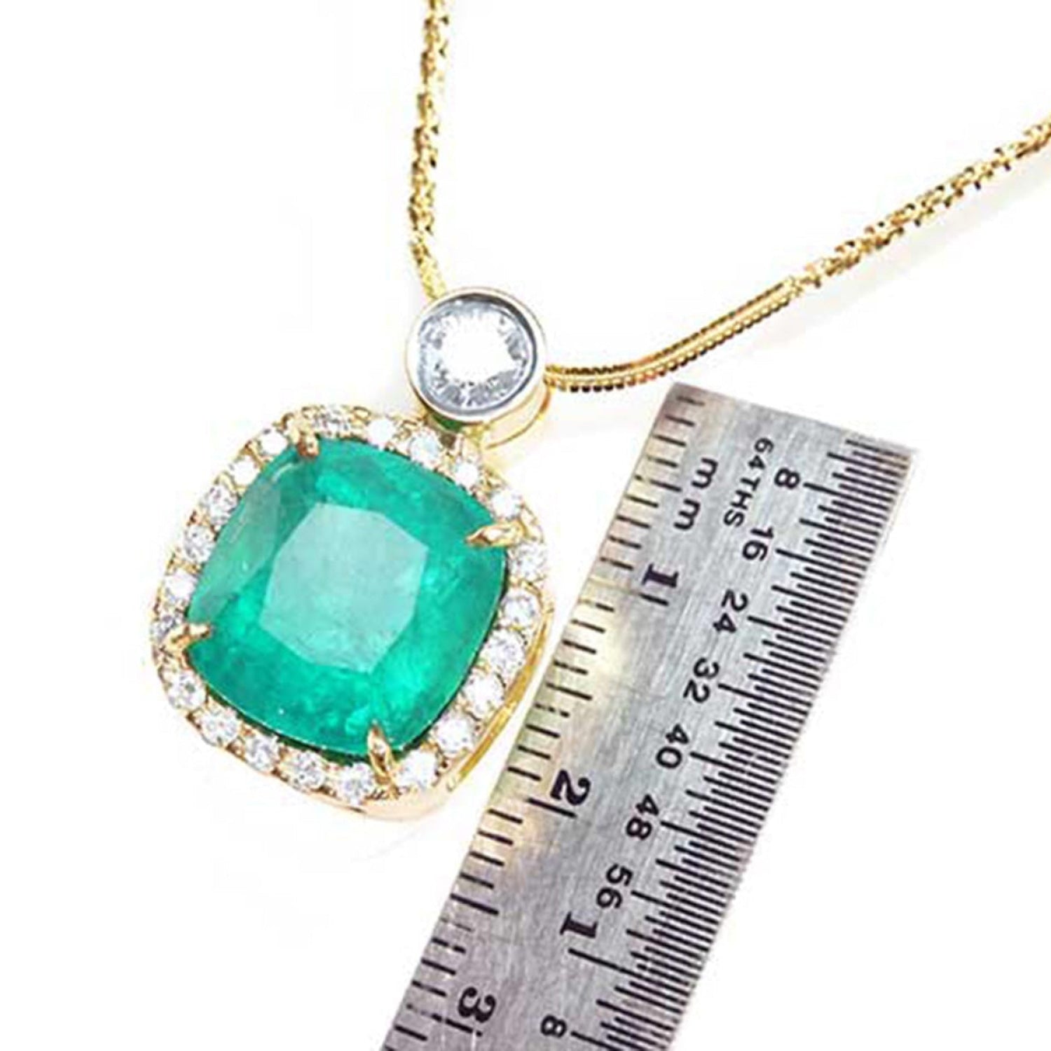 Cushion cut emerald necklace in 18K yellow gold with diamond halo, shown with a ruler for scale.