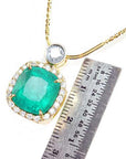 Cushion cut emerald necklace in 18K yellow gold with diamond halo, shown with a ruler for scale.