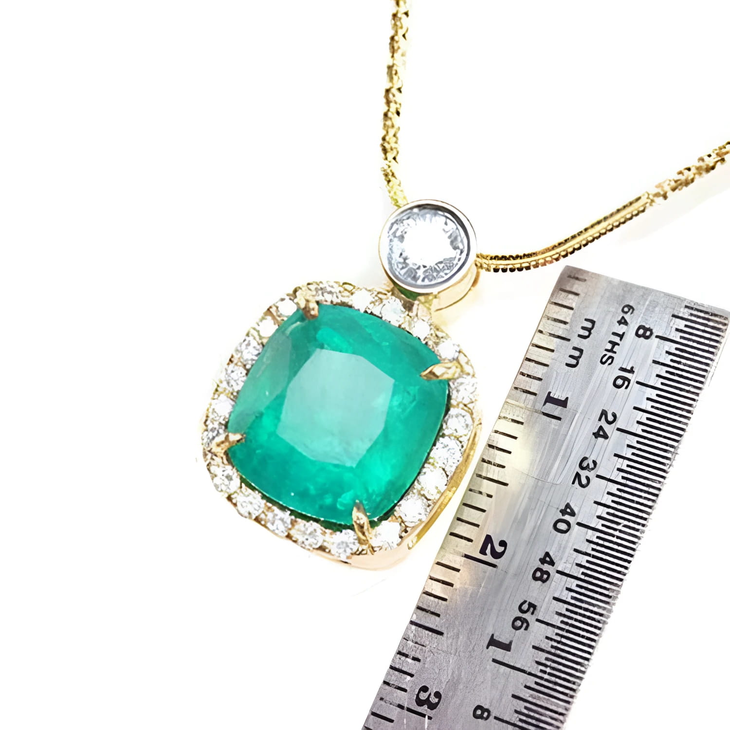 Cushion cut emerald necklace in 18K yellow gold with diamond halo, shown with a ruler for scale.