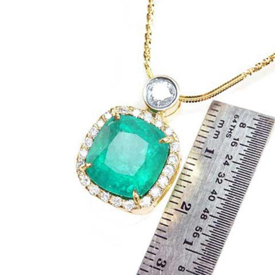 Cushion cut emerald necklace in 18K yellow gold with diamond halo, shown with a ruler for scale.
