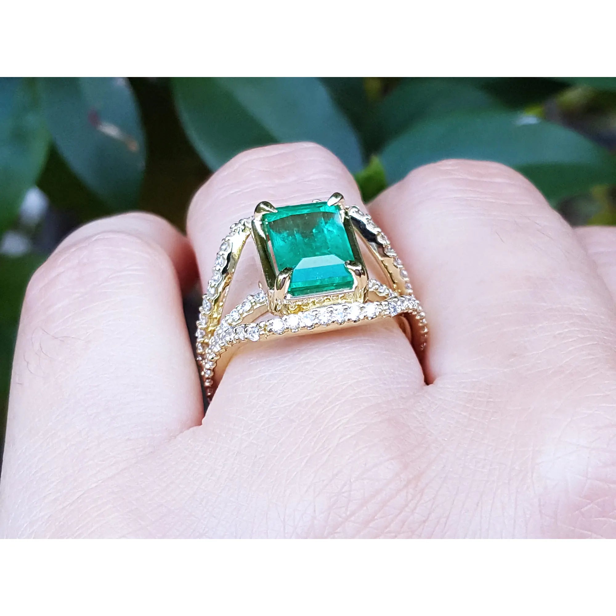 Anillo de oro con esmeralda en mano de mujer sobre un follaje verde.
