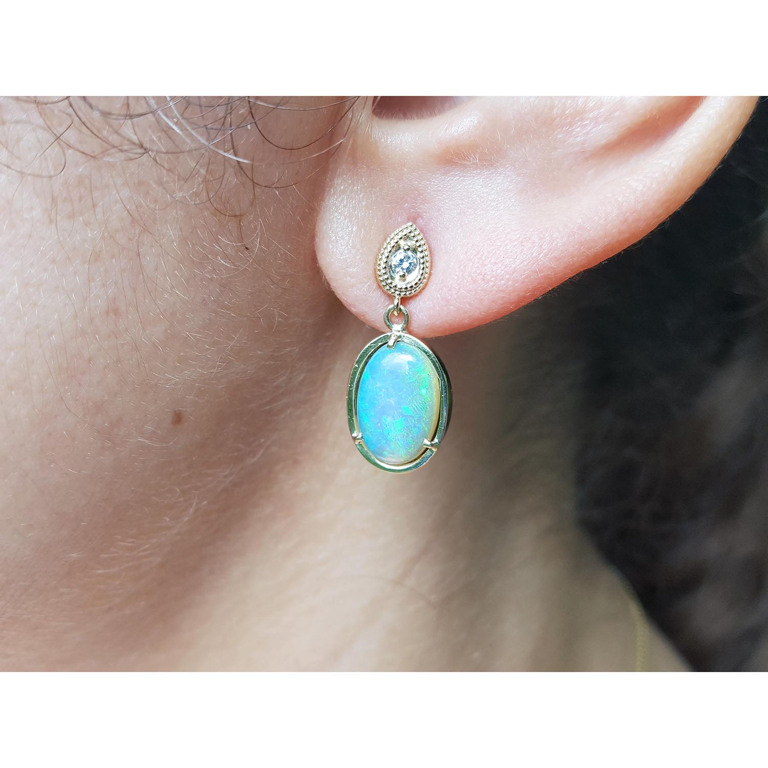Close-up of an ear wearing a gold earring with a blue natural Australian opal.