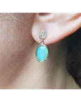 Close-up of an ear wearing a gold earring with a blue natural Australian opal.
