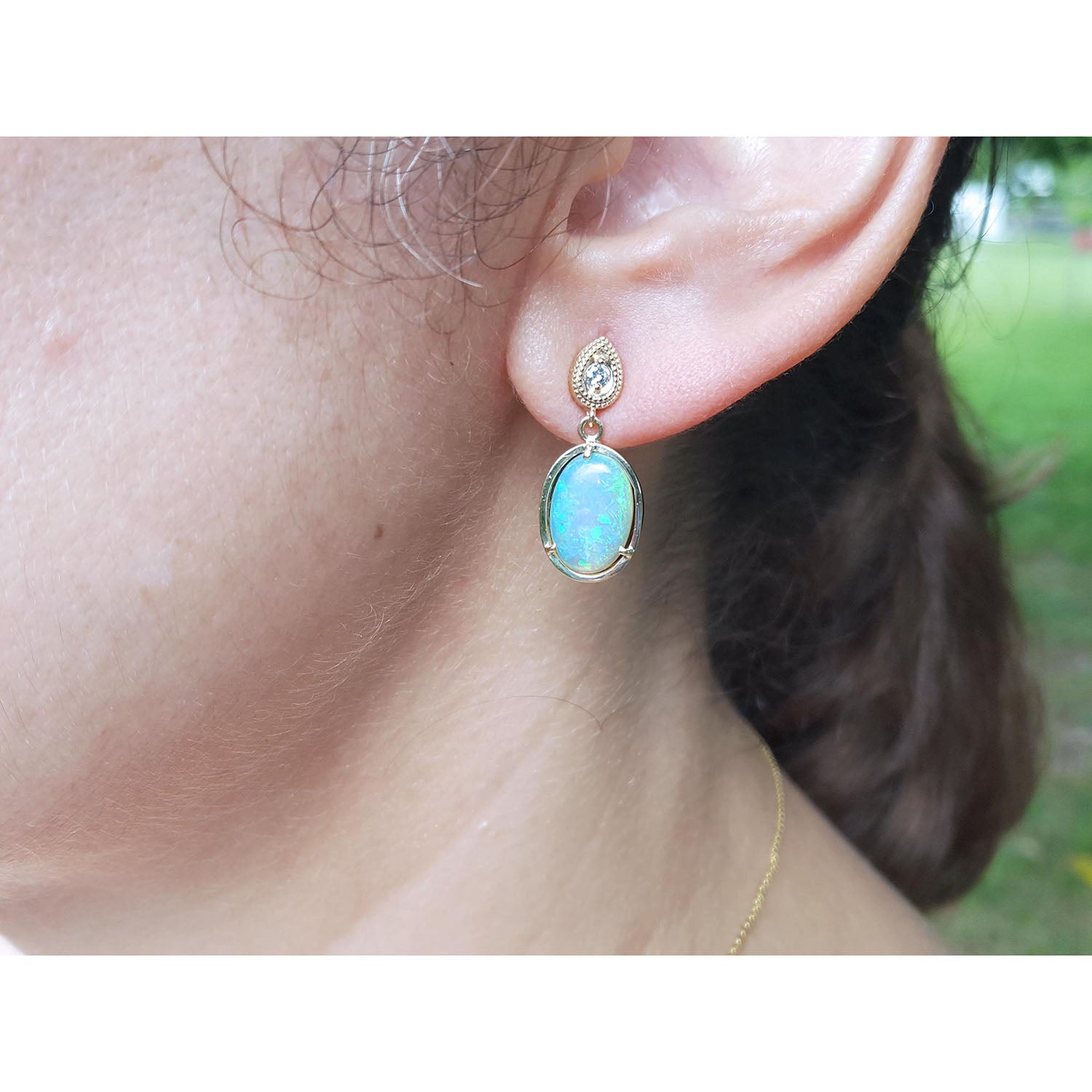 Close-up of an ear wearing a gold earring with a natural Australian opal, on a blurred background.