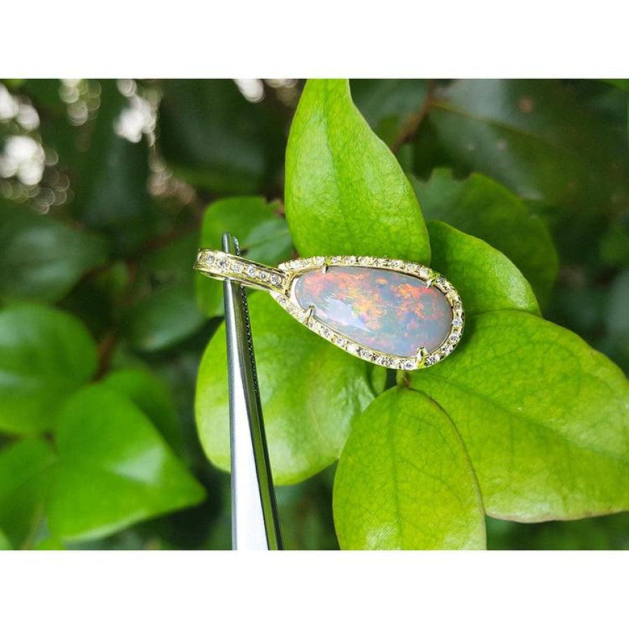 4.30 ct Australian opal pendant with fiery red-orange flashes, halo diamonds, 18K yellow gold, on green leaves.