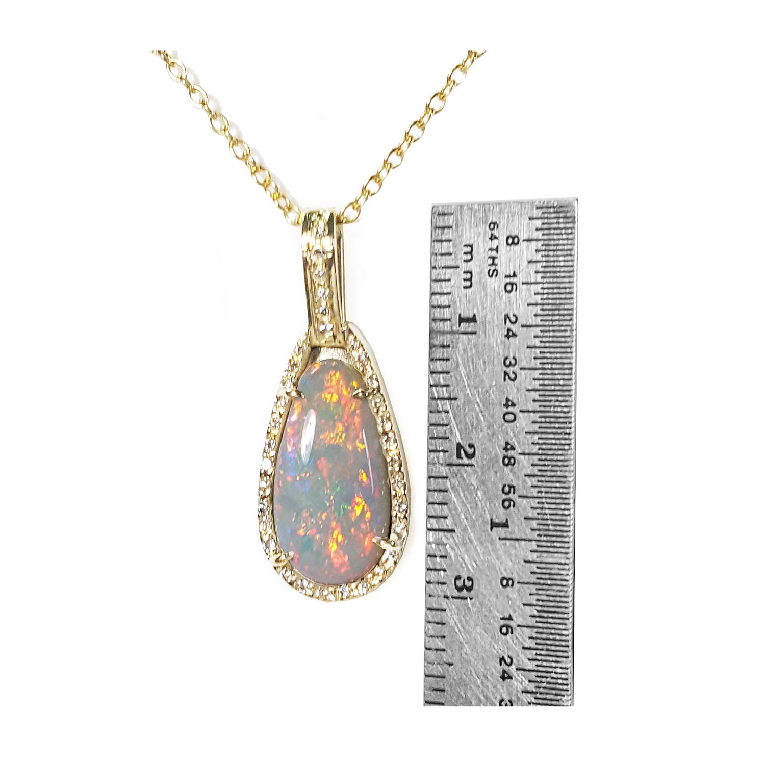 Opal pendant necklace with gold chain next to a ruler for scale on a white background