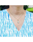 Person wearing a blue and white patterned top with a gold necklace featuring an opal pendant.
