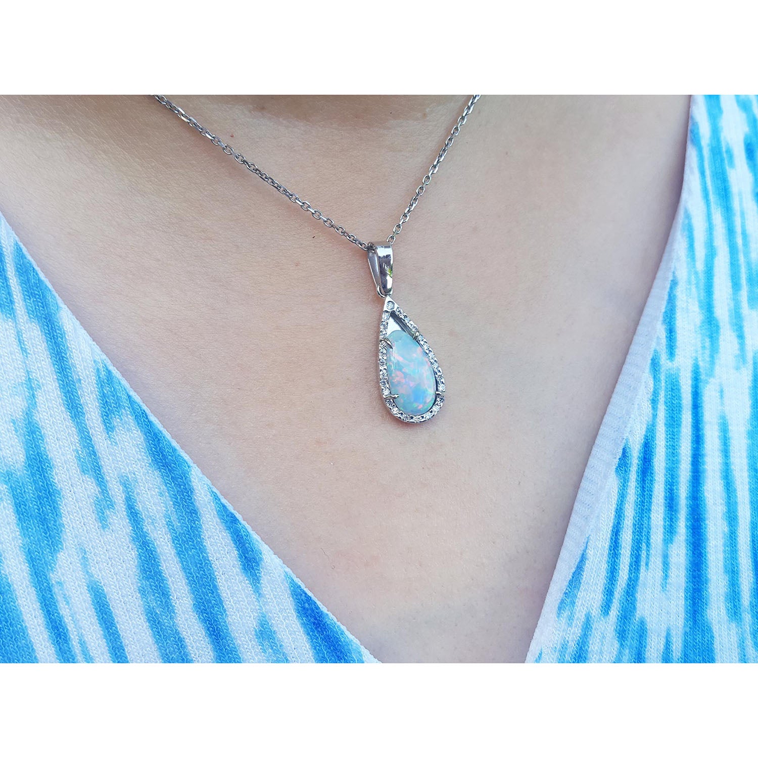 Teardrop-shaped solid opal pendant necklace on a person wearing a blue and white patterned top.