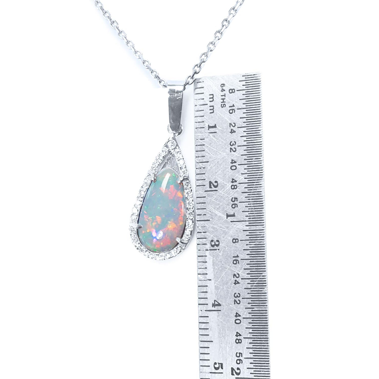 A natural Australian pear shaped opal pendant necklace with a ruler for scale on a white background.