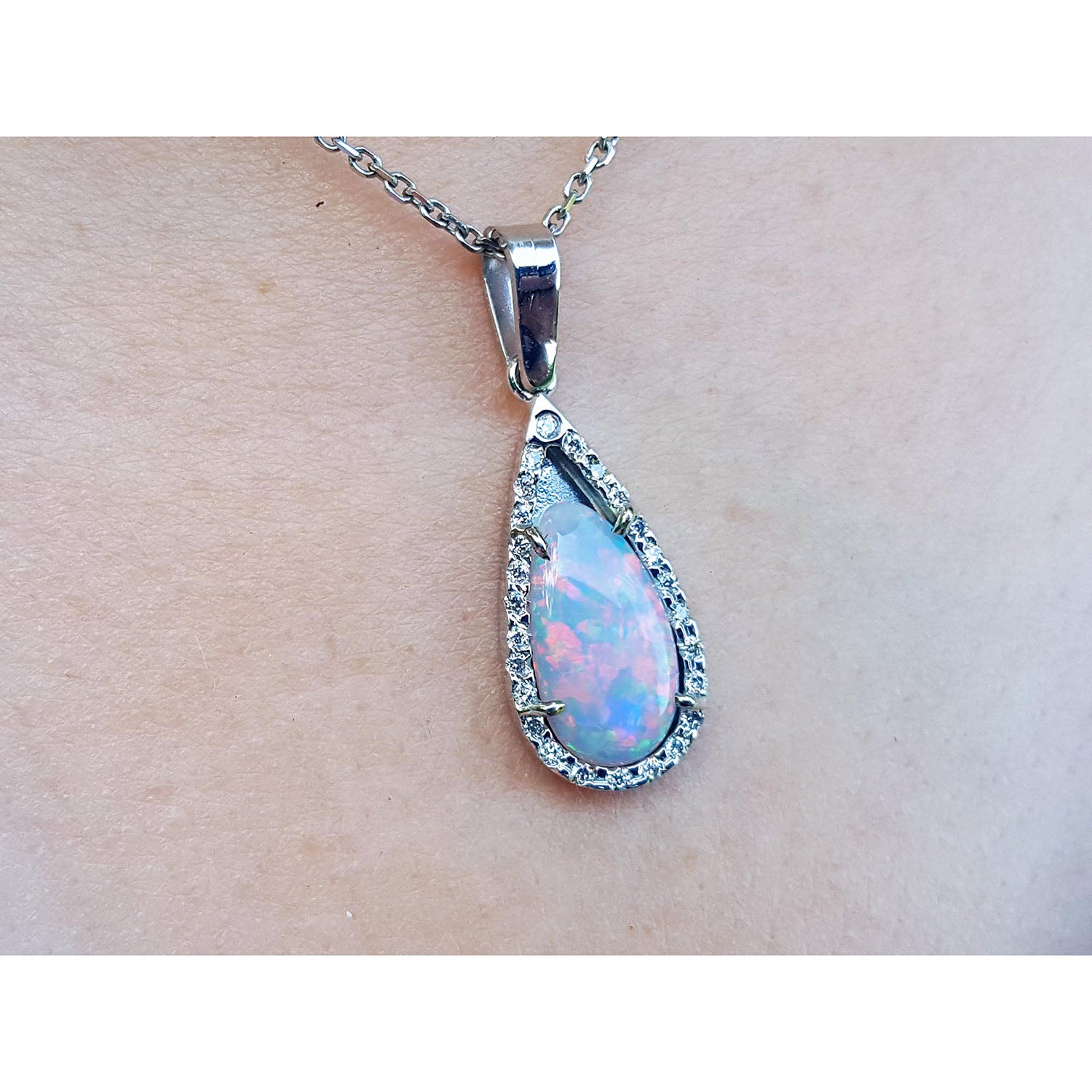 Teardrop-shaped opal pendant on a chain against a skin background.