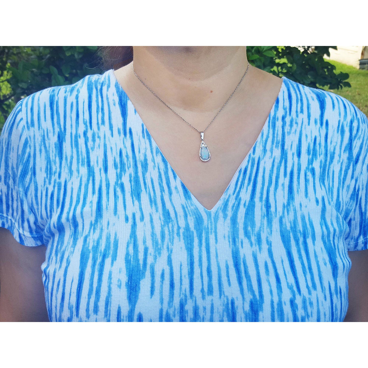 A lady wearing a blue and white tie-dye shirt with a natural opal necklace outdoors.