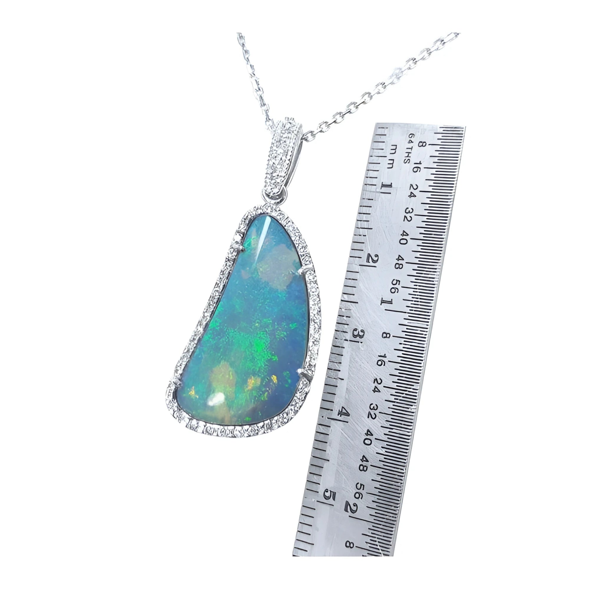 Australian opal pendant with blue-green play of color, halo diamonds, and 18K white gold chain, next to a ruler.