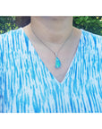 Person wearing a blue and white patterned shirt with a necklace featuring a solid opal pendant.