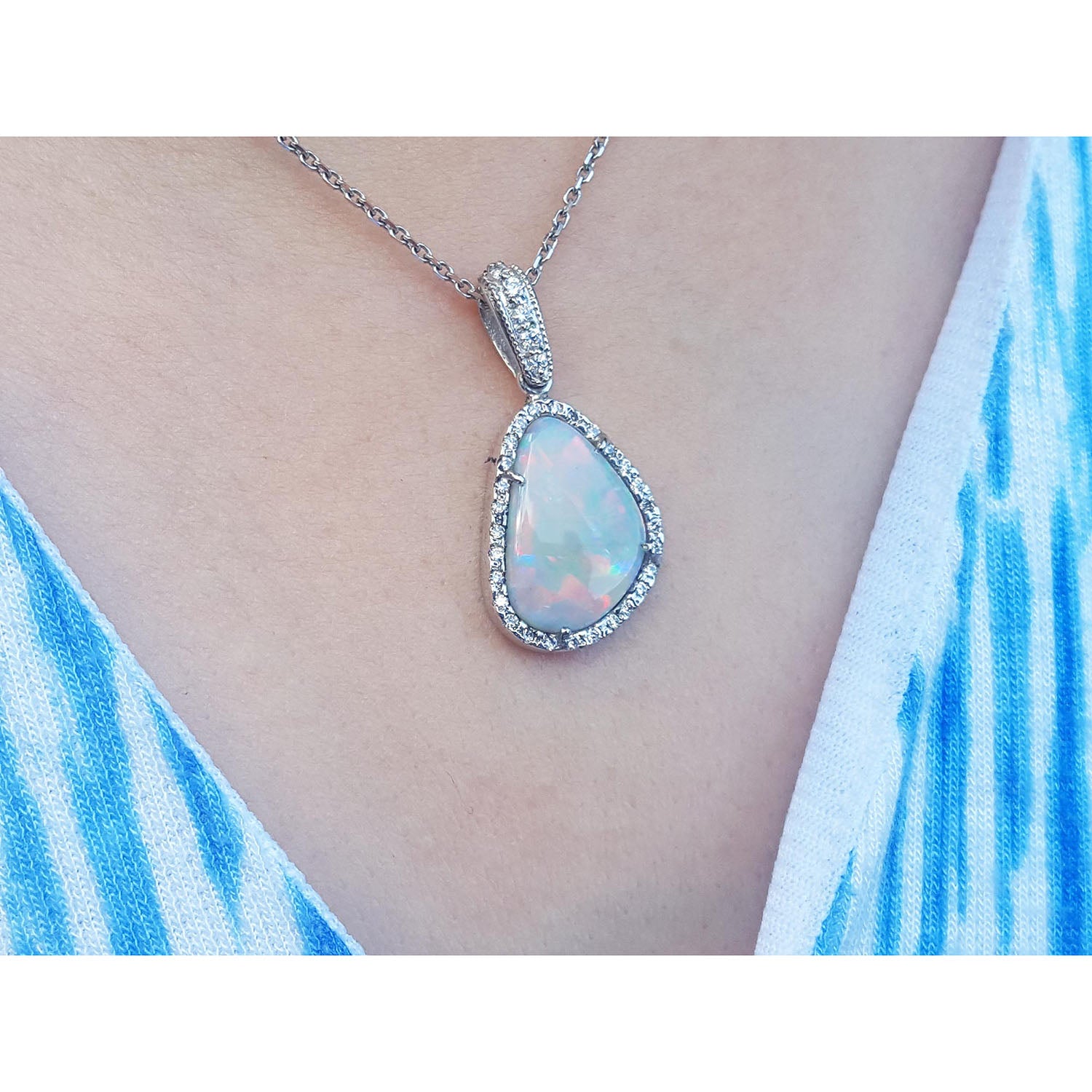 Teardrop-shaped opal pendant on a chain, worn by a person with a blue and white patterned top.