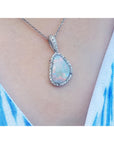 Teardrop-shaped opal pendant on a chain, worn by a person with a blue and white patterned top.