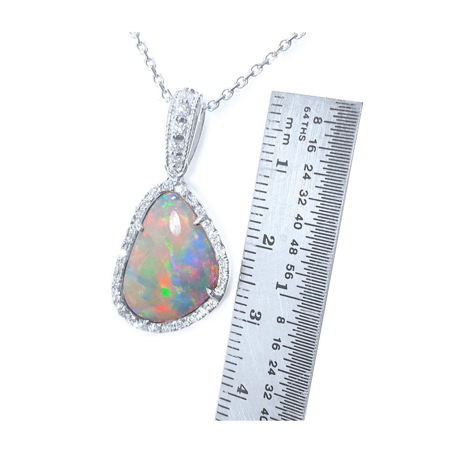 Opal pendant with gold chain next to a ruler on a white background