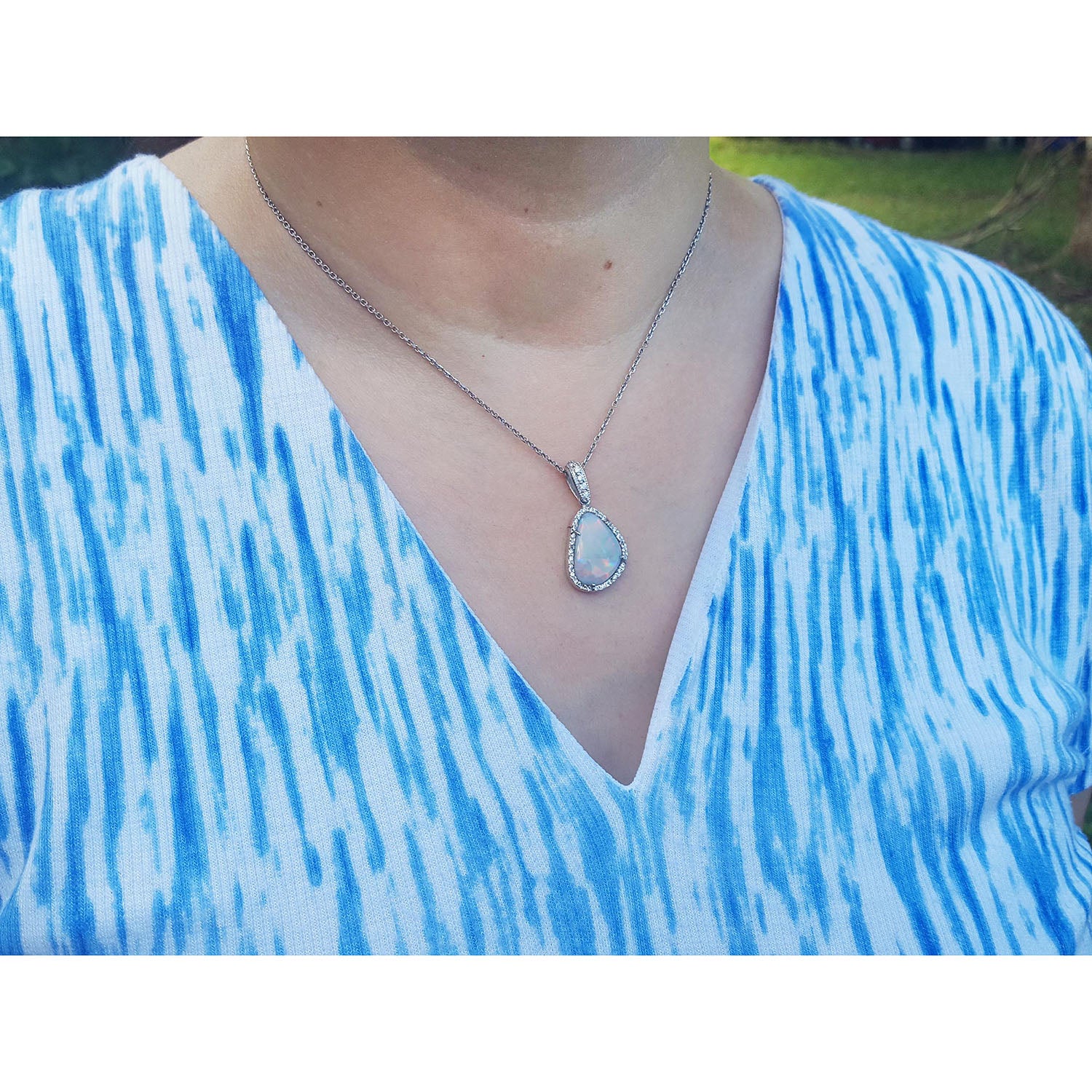 Person wearing a blue and white patterned top with a necklace featuring a teardrop opal pendant.
