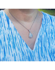 Person wearing a blue and white patterned top with a necklace featuring a teardrop opal pendant.