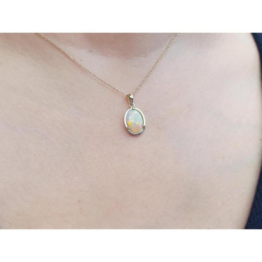Oval white Australian opal pendant in 14k yellow gold on a delicate chain, worn on a person.
