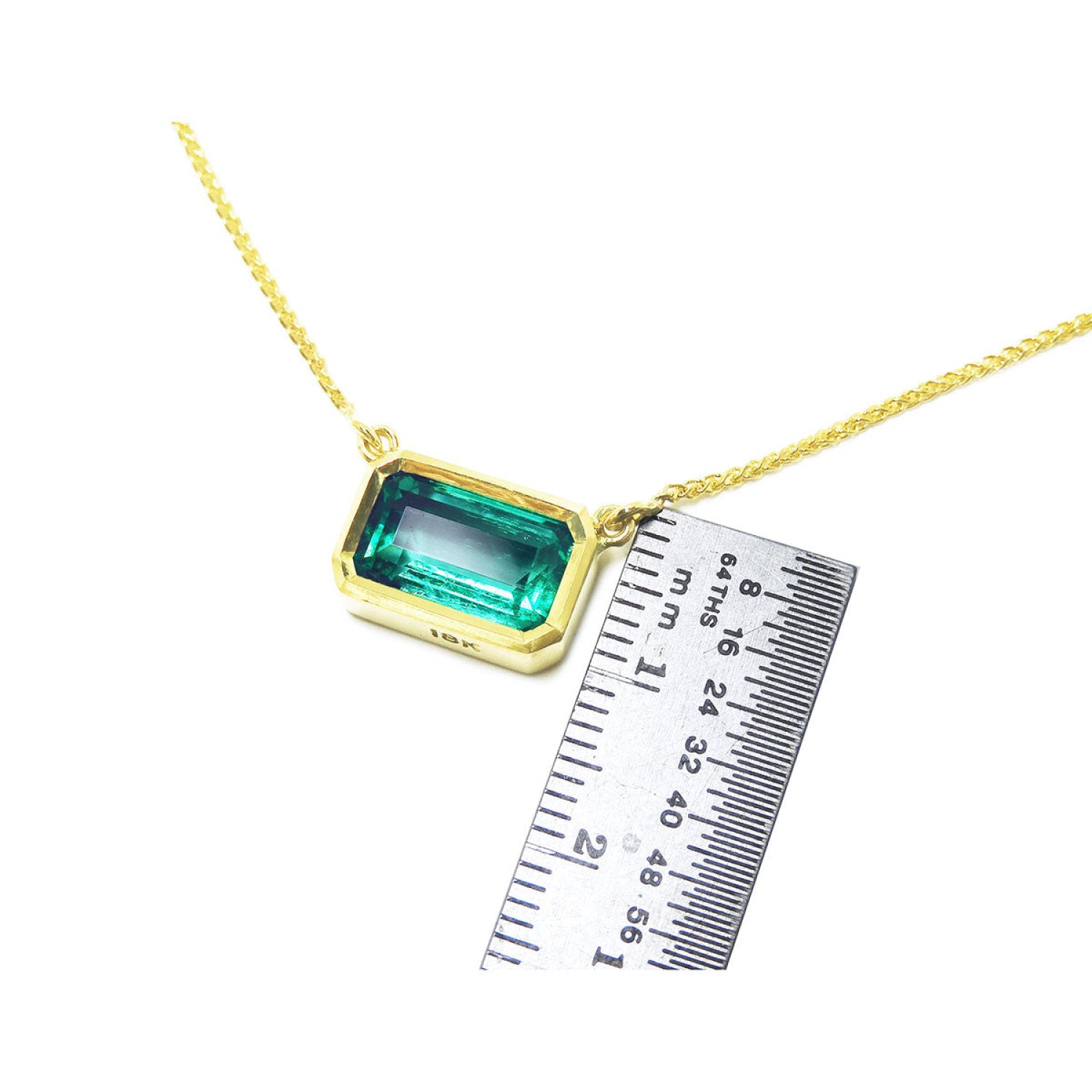 East-west emerald-cut solitaire emerald necklace in 18K yellow gold, shown with a ruler for scale.