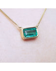 East-west emerald-cut solitaire emerald necklace in 18K yellow gold, bezel set.