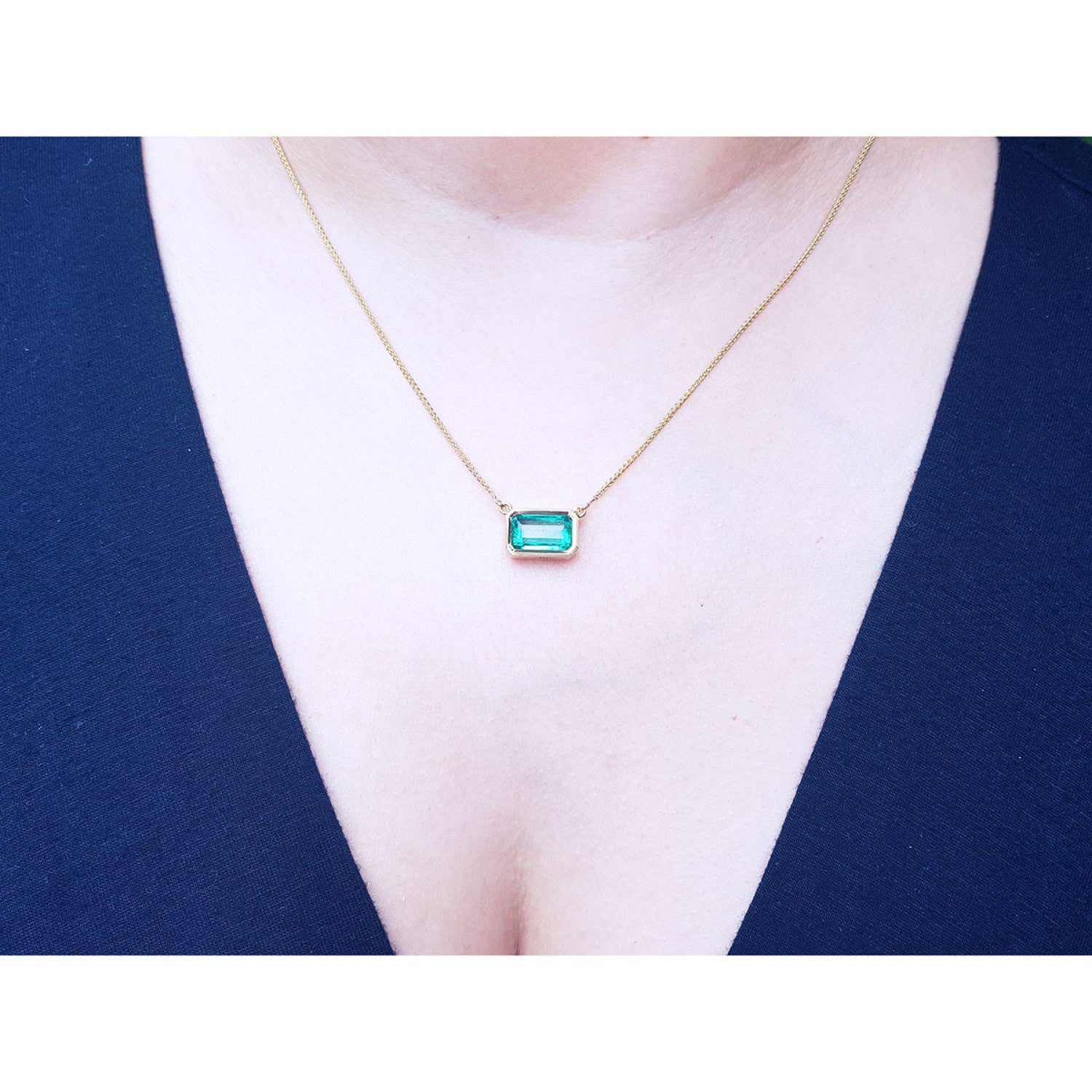 East-west rectangular emerald solitaire necklace in 18K yellow gold, worn on a person.