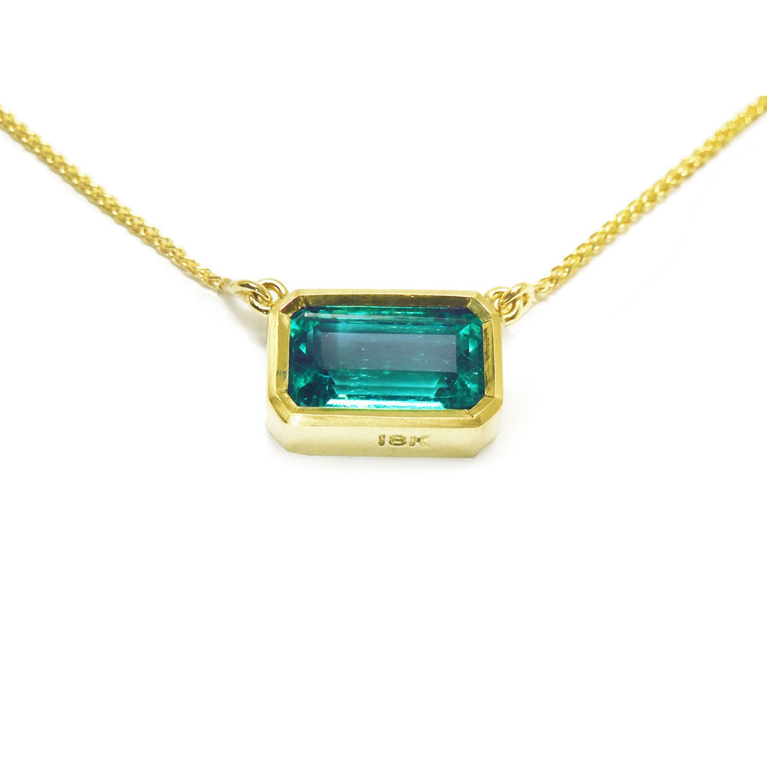 East-west rectangular emerald solitaire necklace in 18K yellow gold with a vibrant bluish-green stone.