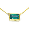 East-west rectangular emerald solitaire necklace in 18K yellow gold with a vibrant bluish-green stone.