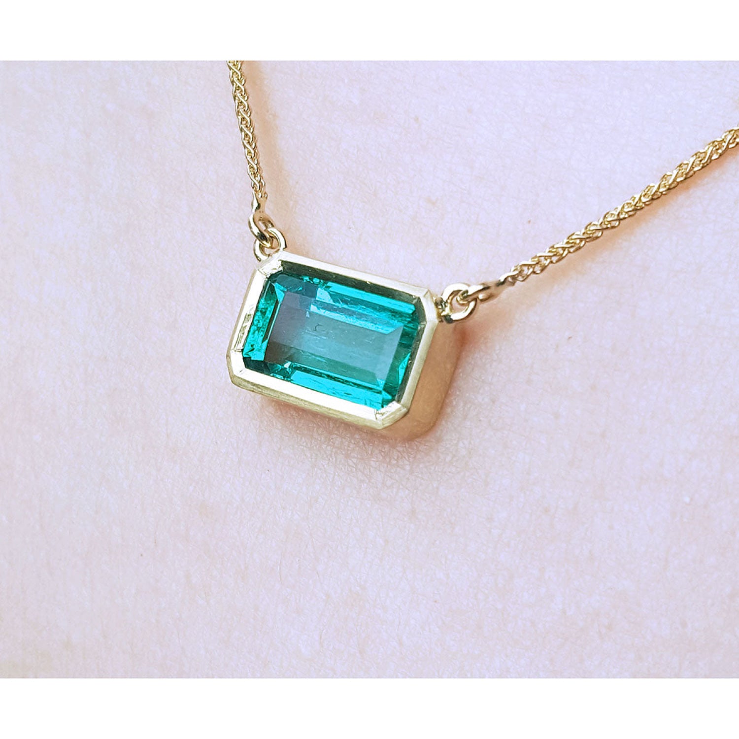 East-west emerald-cut Colombian emerald solitaire necklace in 18K yellow gold.