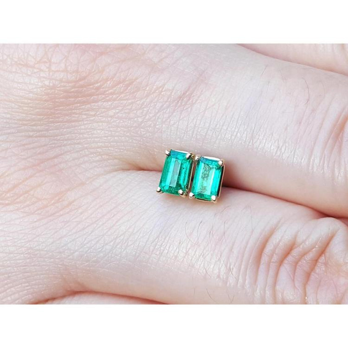 Pair of emerald cut emerald stud earrings, 0.78 ct, in 14K yellow gold basket settings.
