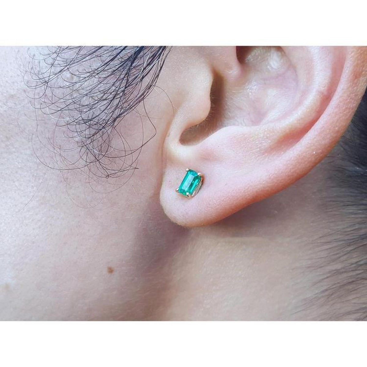 Emerald cut emerald stud earring in 14K yellow gold on an earlobe.