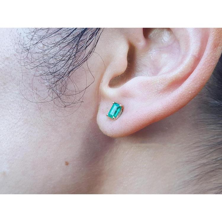 Emerald cut emerald stud earring in 14K yellow gold on an earlobe.