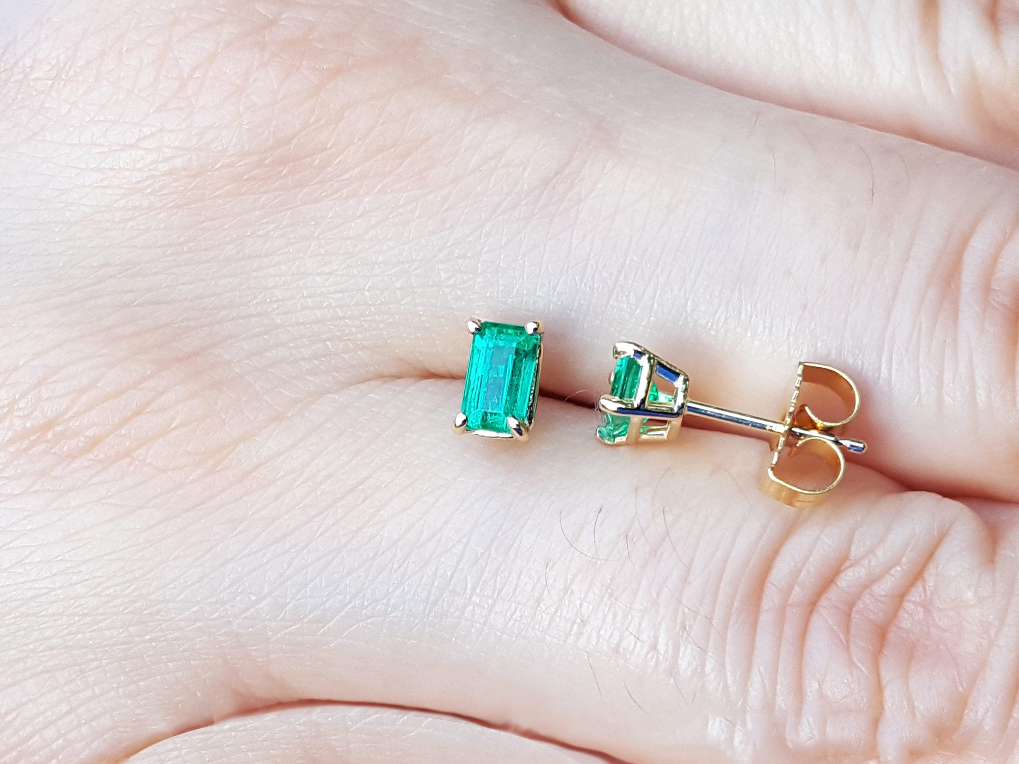 14k Yellow gold emerald solitaire stud earrings on a hand.