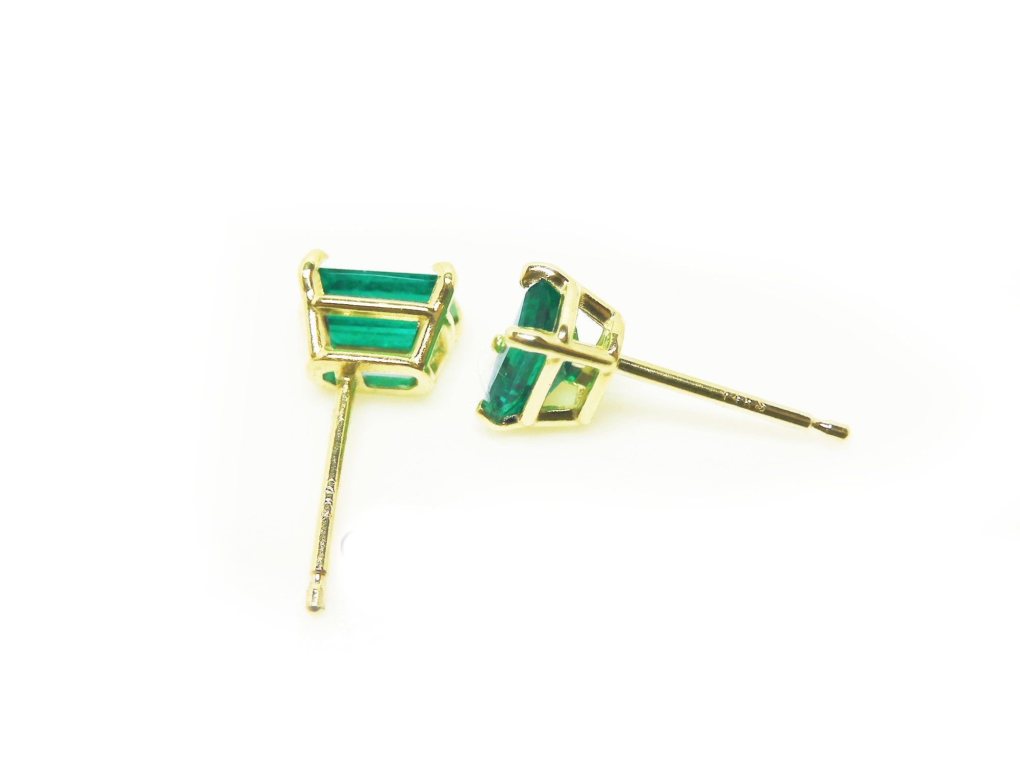Pair of emerald gemstone earrings with gold settings on a side profile view.