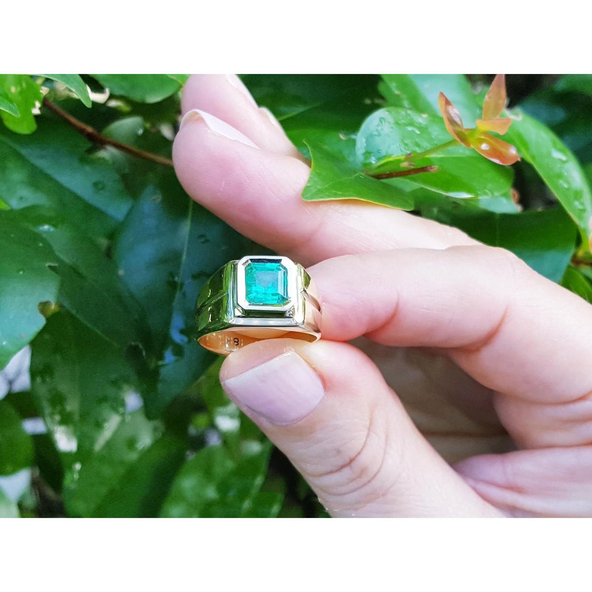 Gold ring with a real emerald held between fingers against a leafy background