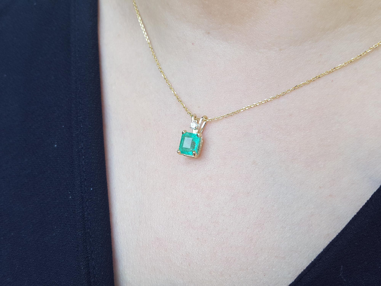 Gold necklace with a square emerald pendant on a person wearing a dark top.