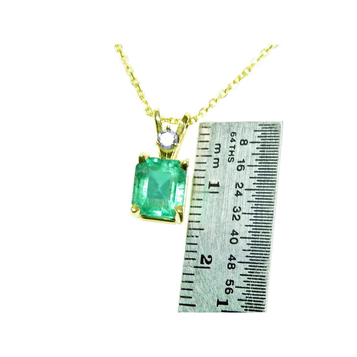 Gold pendant with a natural emerald-cut emerald next to a ruler for size reference on a white background.
