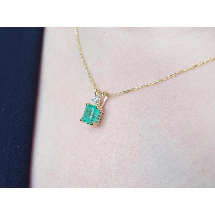 Gold necklace with a Muzo colombian emerald pendant on a person's neck.