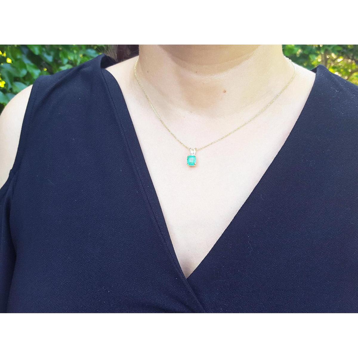 A woman wearing a navy-blue top with a gold necklace featuring a natural emerald pendant.