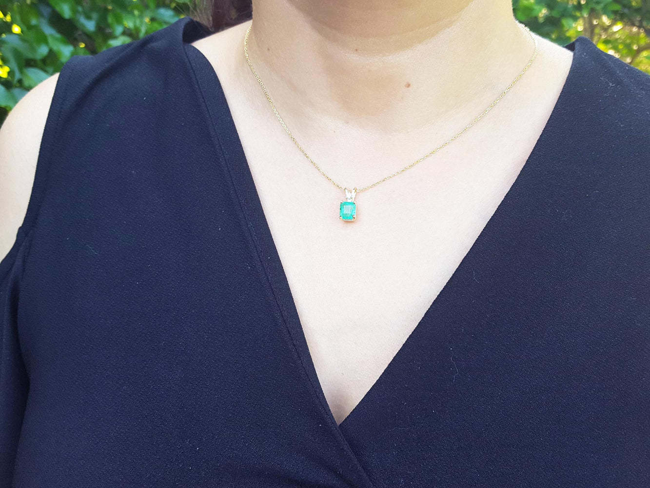A woman wearing a navy-blue top with a gold necklace featuring a natural emerald pendant.