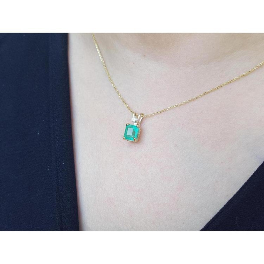 Emerald-cut emerald pendant in 14K yellow gold with diamond accent, worn on a woman's neck.