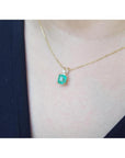 Emerald-cut emerald pendant in 14K yellow gold with diamond accent, worn on a woman's neck.